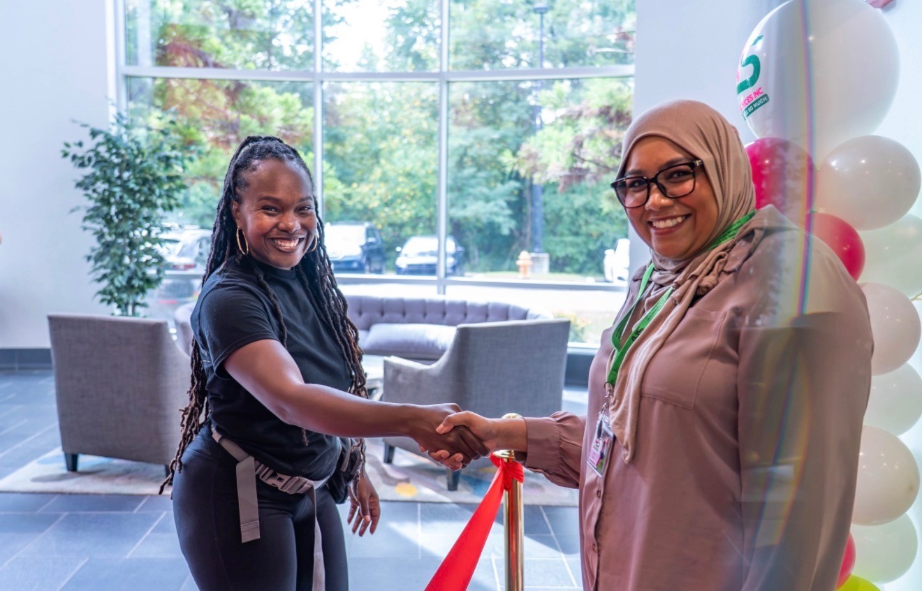 Fayola Whyte-Manco shaking hands with a client beside the red ribbon and balloon column at the Able Health Services grand opening