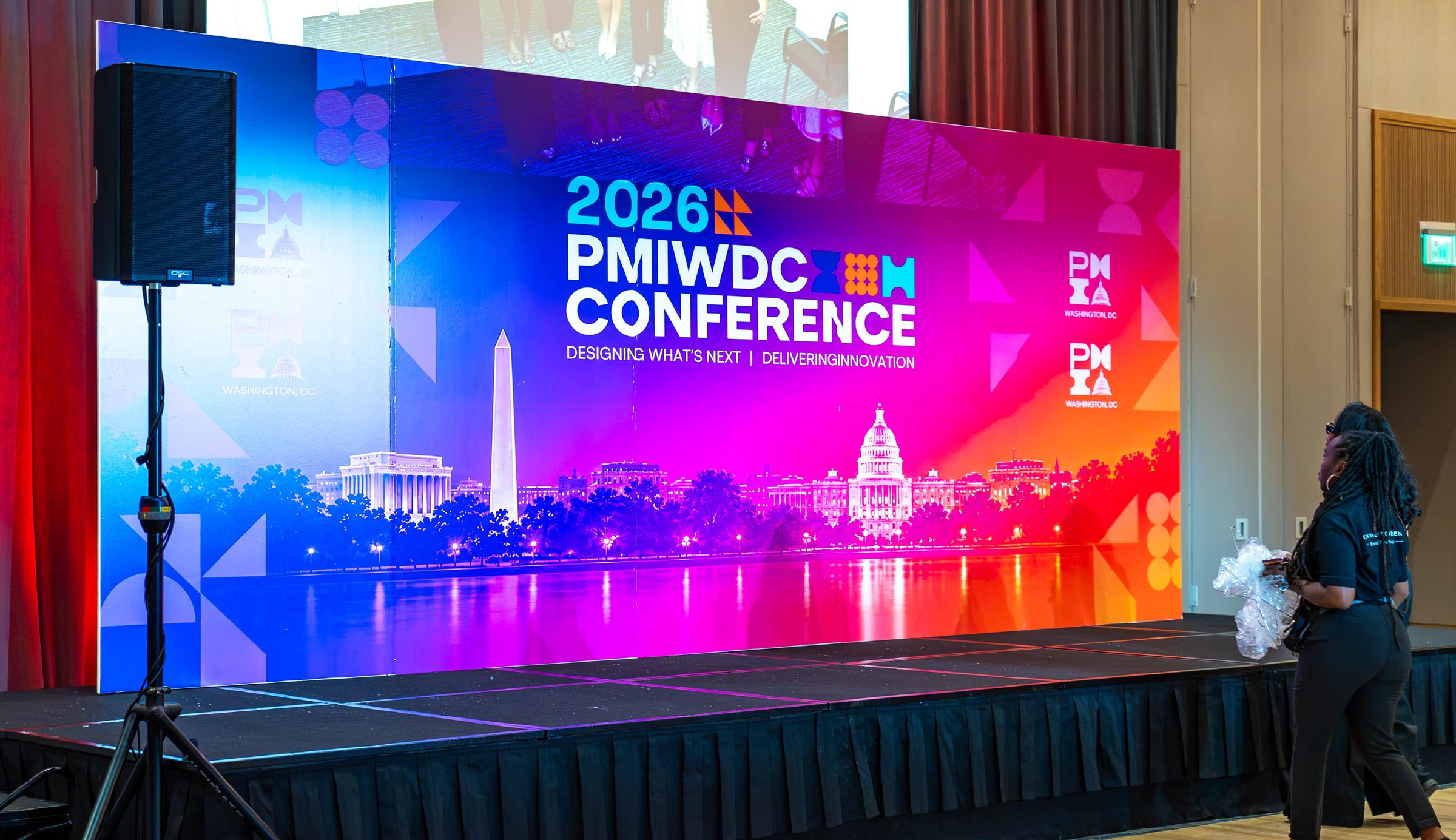 The 2026 PMIWDC Conference stage, its wide screen glowing magenta and blue between red-lit curtains, at the PMI Washington DC Chapter Awards Gala