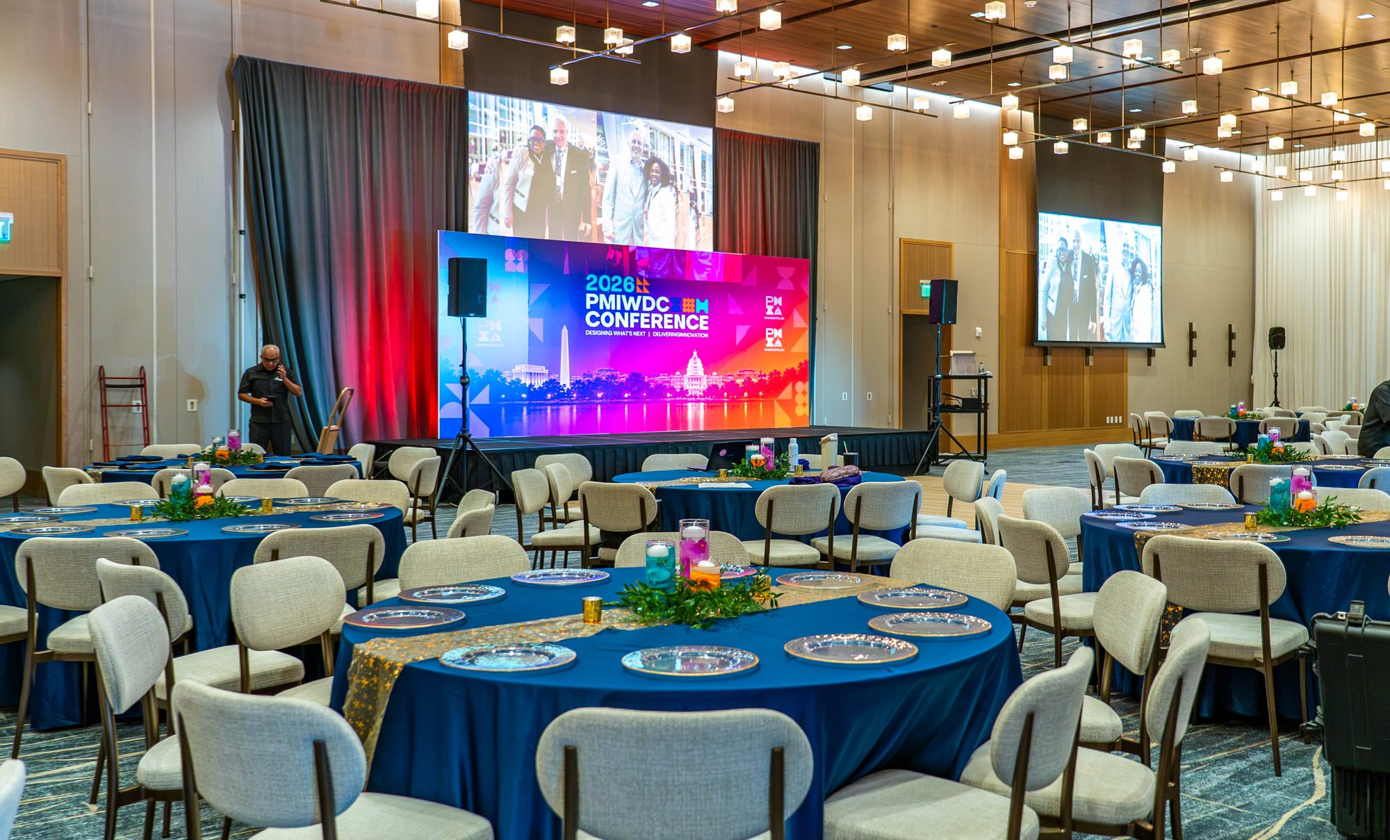 Finished ballroom with navy tables, orchid centerpieces and the lit 2026 PMIWDC Conference stage for the PMI Washington DC Chapter Awards Gala, JW Marriott Reston, Virginia