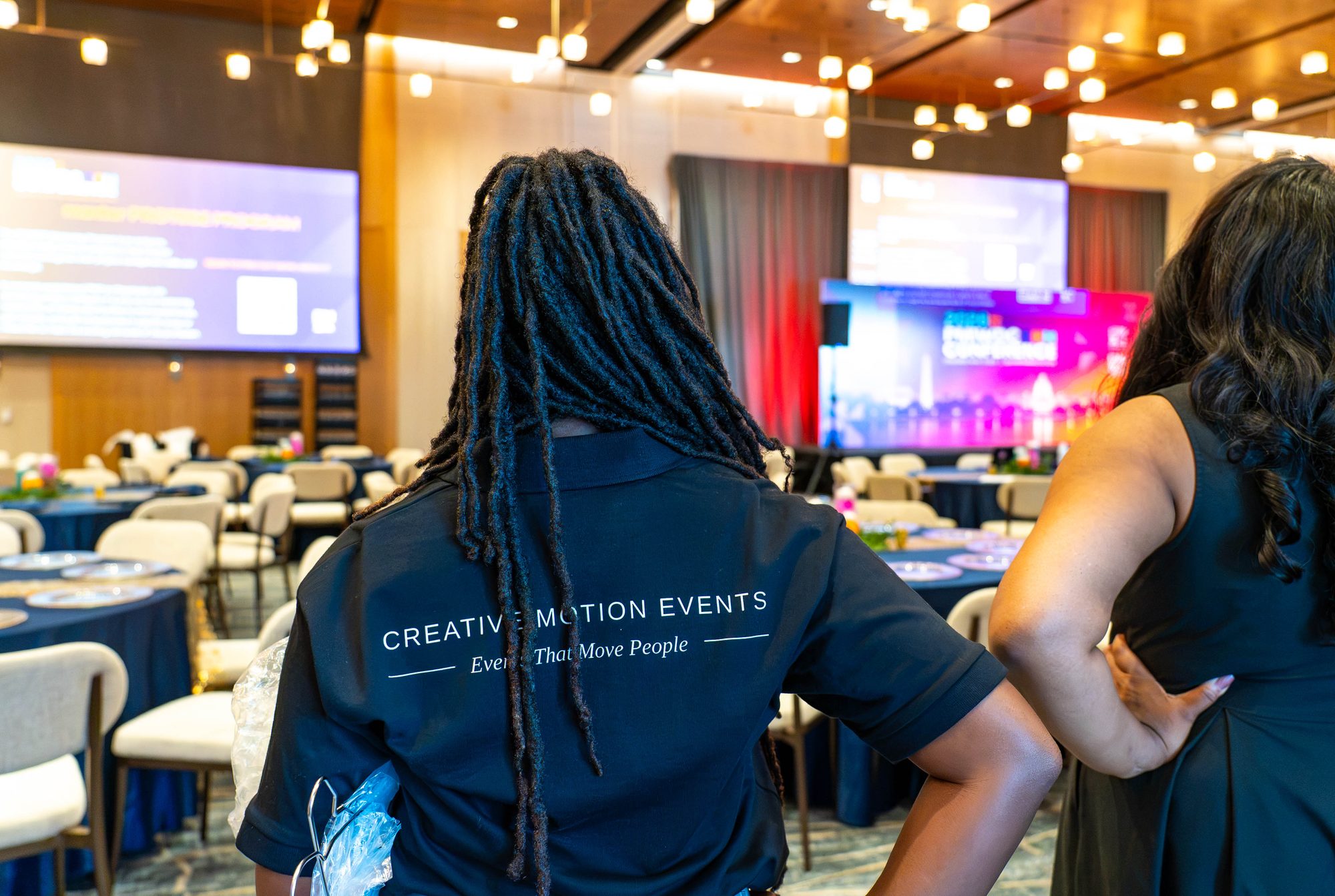 Creative Motion Events planner, seen from behind in a branded shirt, overlooking the finished ballroom and lit stage at the PMI Washington DC Chapter Awards Gala, JW Marriott Reston, Virginia