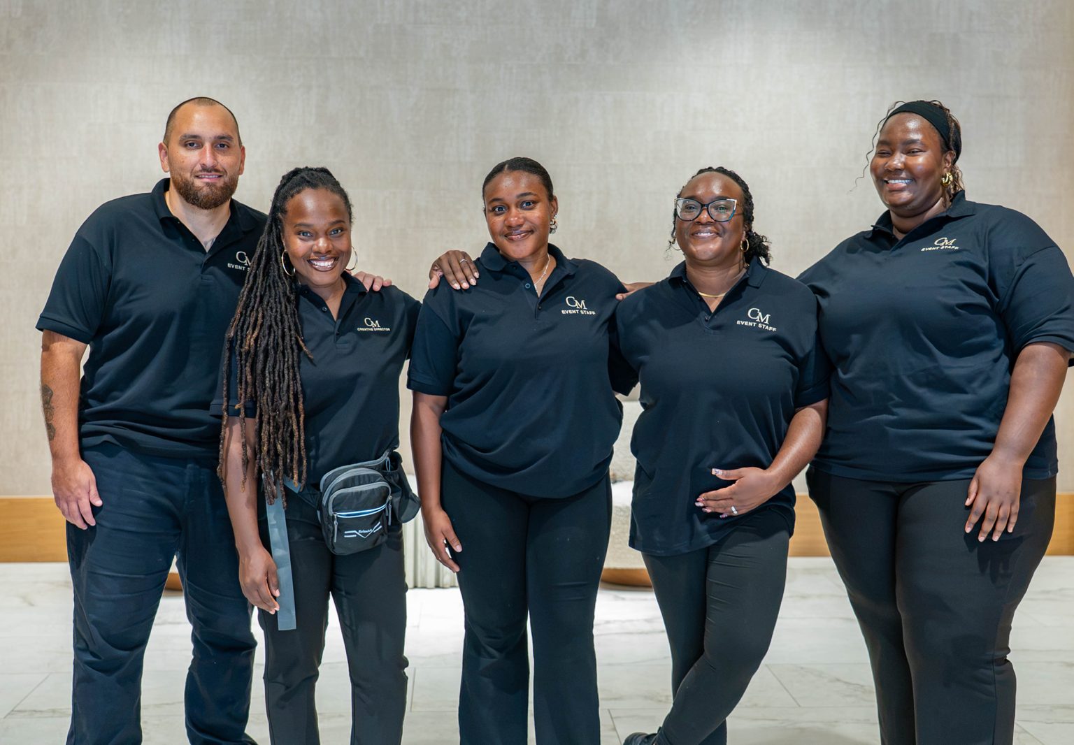 Five event staff in black polo shirts posing together in front of a balloon installation