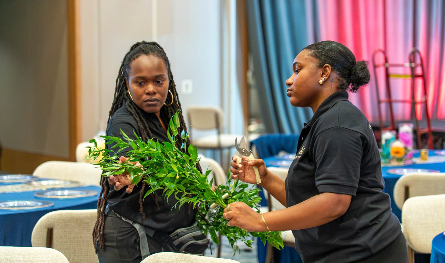 Two event staff in black shirts arranging greenery with floral shears
